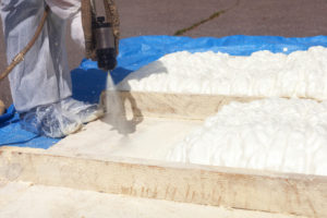 Technician spraying foam insulation using Plural Component Spray Gun. Spraying polyurethane foam for roof